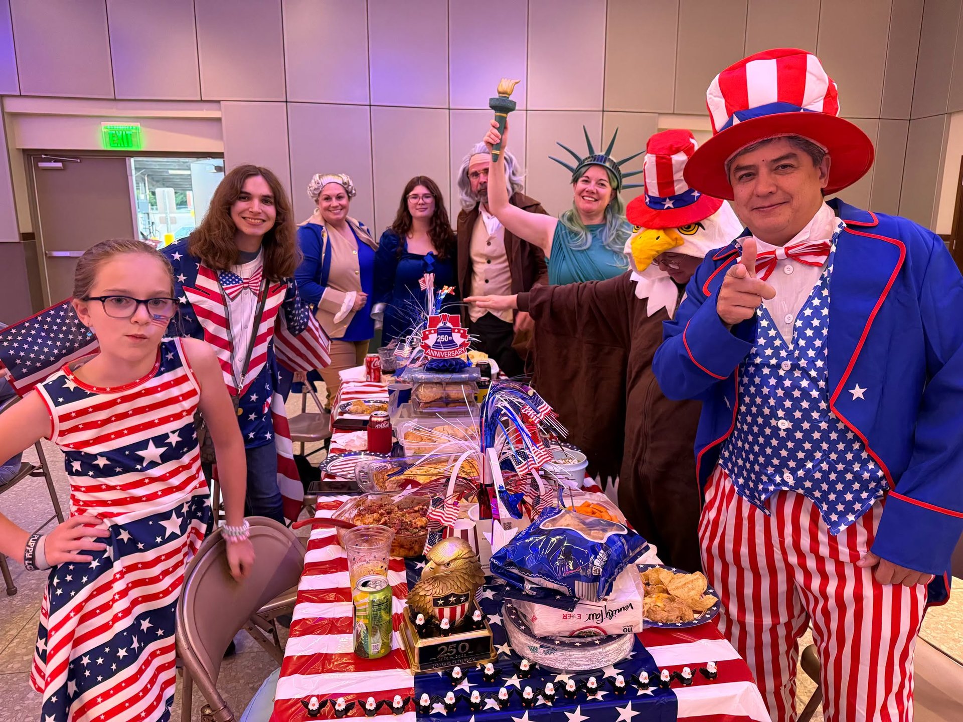 A performer in an Uncle Sam suit and top hat points at the camera beside a table of guests in patriotic dress at the Murder Mystery Night in the IBEW Local 1 hall.